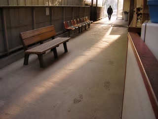 空いた木のベンチ(休憩の途中)。背景に人物が一人写る