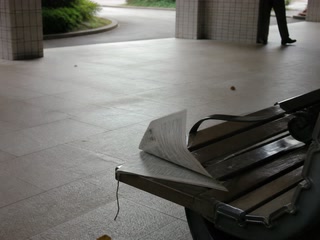風でめくれた新聞(移動の途中)。背景に人物が一人写る