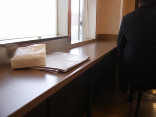 薄い紙袋と新聞(休憩の途中)。背景に人物が一人写る
