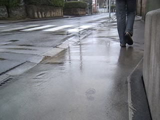 駅へ続く濡れた舗装路(少し足を止めた時)。背景に人物が一人写る