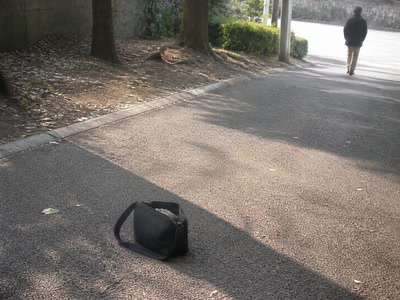 長く伸びた影と鞄（少し足を止めた時）。背景に人物が一人写る
