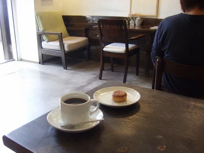 珈琲と小さな焼き菓子（椅子へ座った後）。背景に人物が一人写る