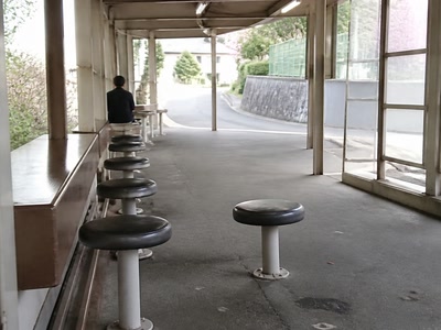 空いた丸椅子（帰り支度の前）。背景に人物が一人写る