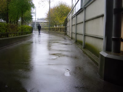 駅へ続く濡れた舗装路（鞄を持ち直した時）。背景に人物が一人写る