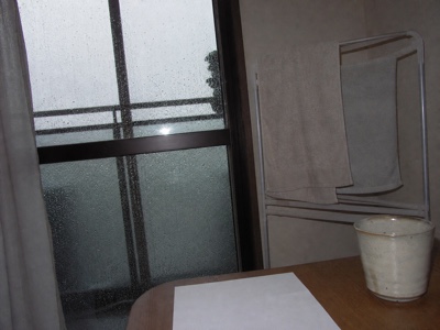 雨粒の付いた窓と室内の物干しと湯のみ