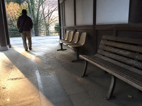 空いた木のベンチ（人の流れが切れた時）。背景に人物が一人写る