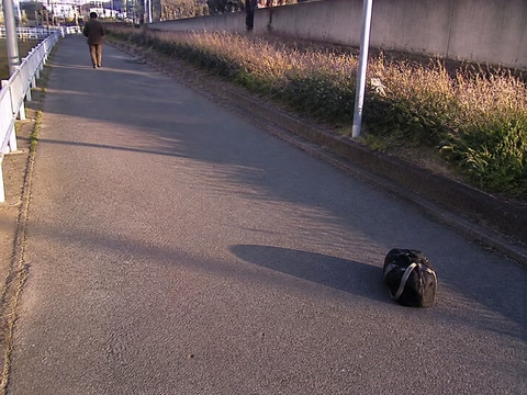 長く伸びた影と鞄（鞄を持ち直した時）。背景に人物が一人写る