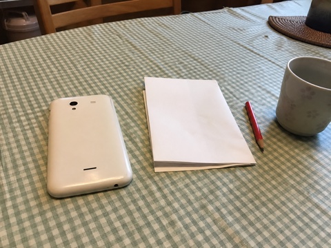 食卓に伏せた古い携帯電話と白い紙と赤鉛筆