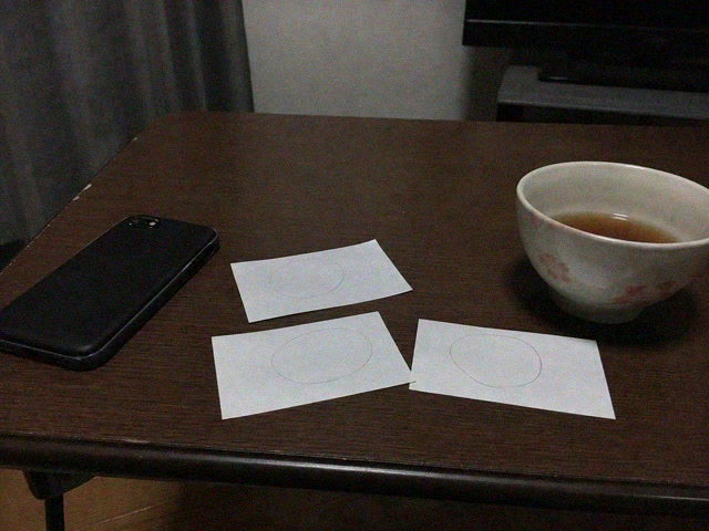 三枚の紙に書いた丸と伏せた携帯電話と茶