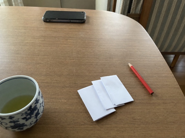 食卓に置いた白い紙と赤鉛筆と伏せた携帯電話